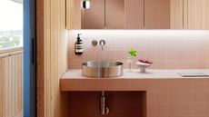 A bathroom with pink square tiles, wood panelled walls, and a steel sink