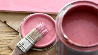 Tin of pink paint with lid and brush on floor