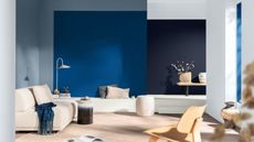 Image of a modern, open living room with walls that are painted in a mix of light blue, bright mid blue, and navy blue. There is an off-white sofa and white bench seating. There are blue and neutral decor accents around the room.