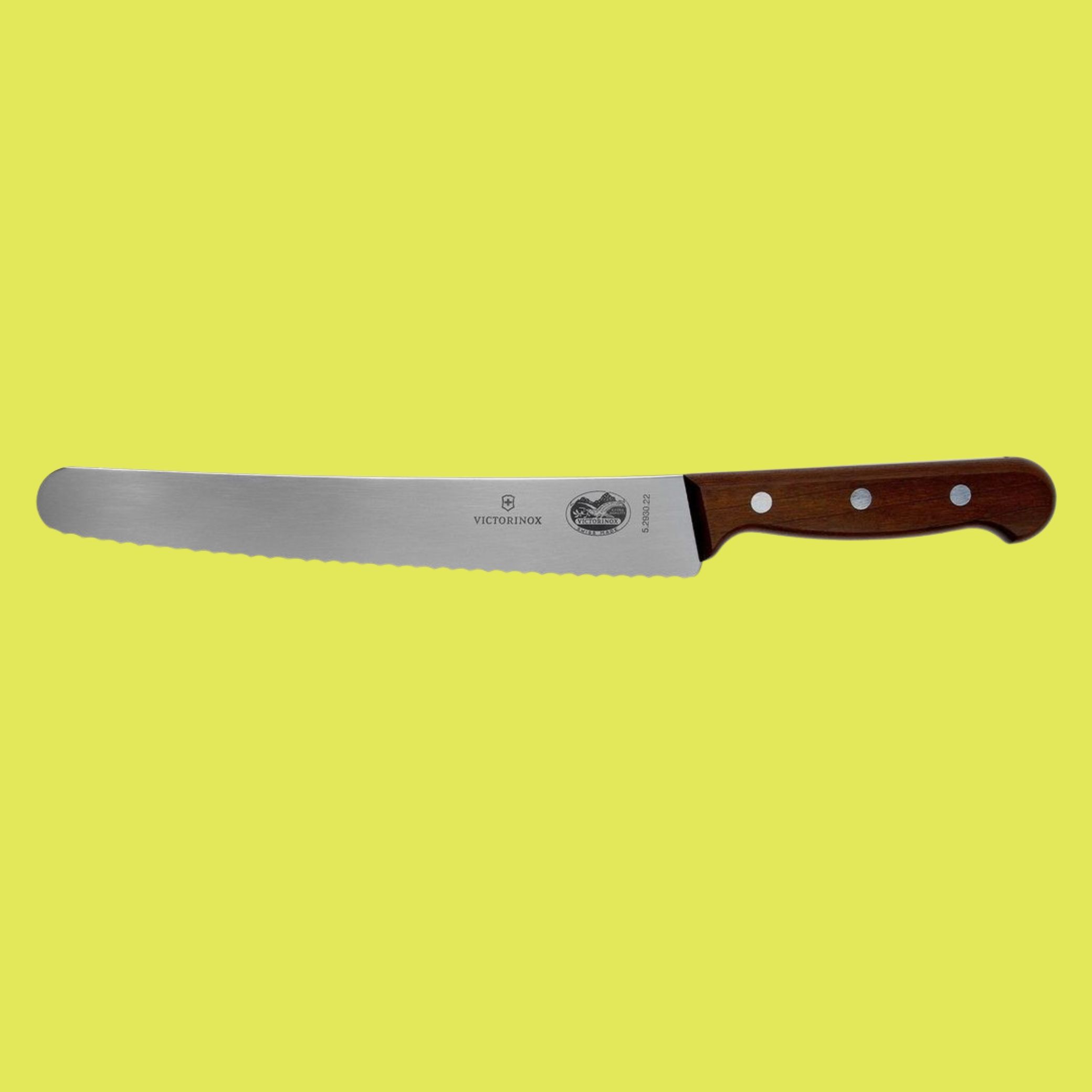 A bread knife with rosewood handle and three silver spots sints against bright yellow background horizontally.
