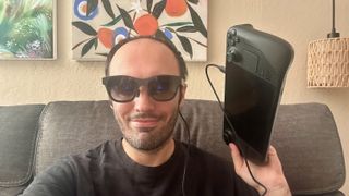 A selfie of the author wearing XREAL Air 2 AR glasses tethered to a Steam Deck held in his left hand next to his face.