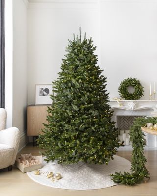 A white minimalist living room with a pre-lit Christmas tree next to a fireplace