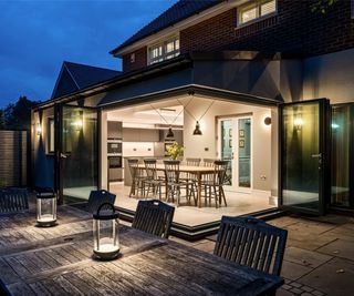 Extension to brick-clad house shown at night, with bifold doors open revealing a kitchen diner