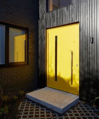 oversized yellow front door on house with vertical black cladding