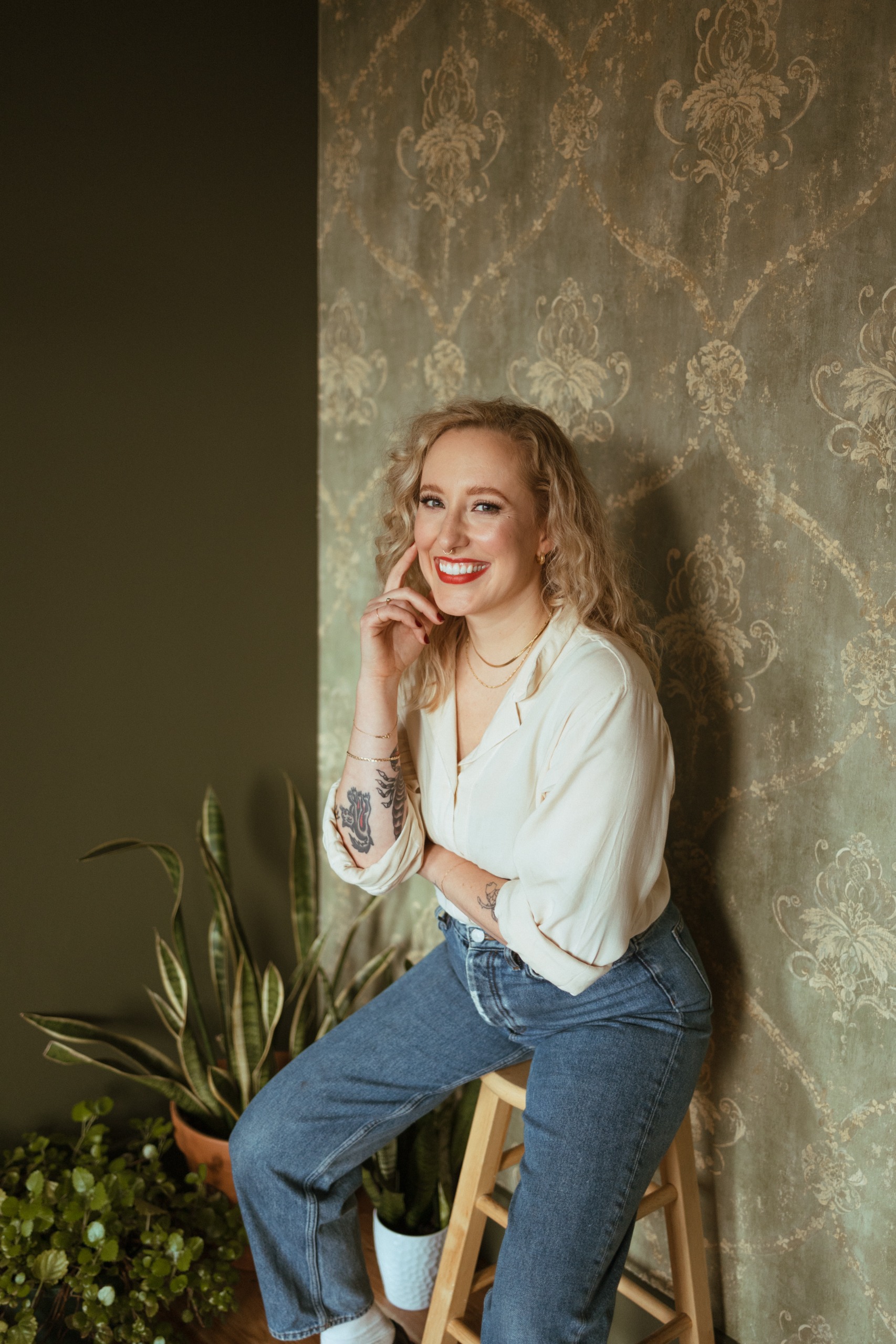 a white woman with blonde hair and tattoos in a white shirt and blue jeans