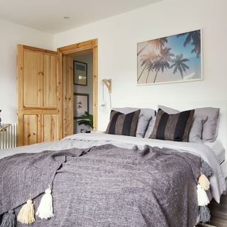 bedroom with white wall and grey bed with cushions and wooden door