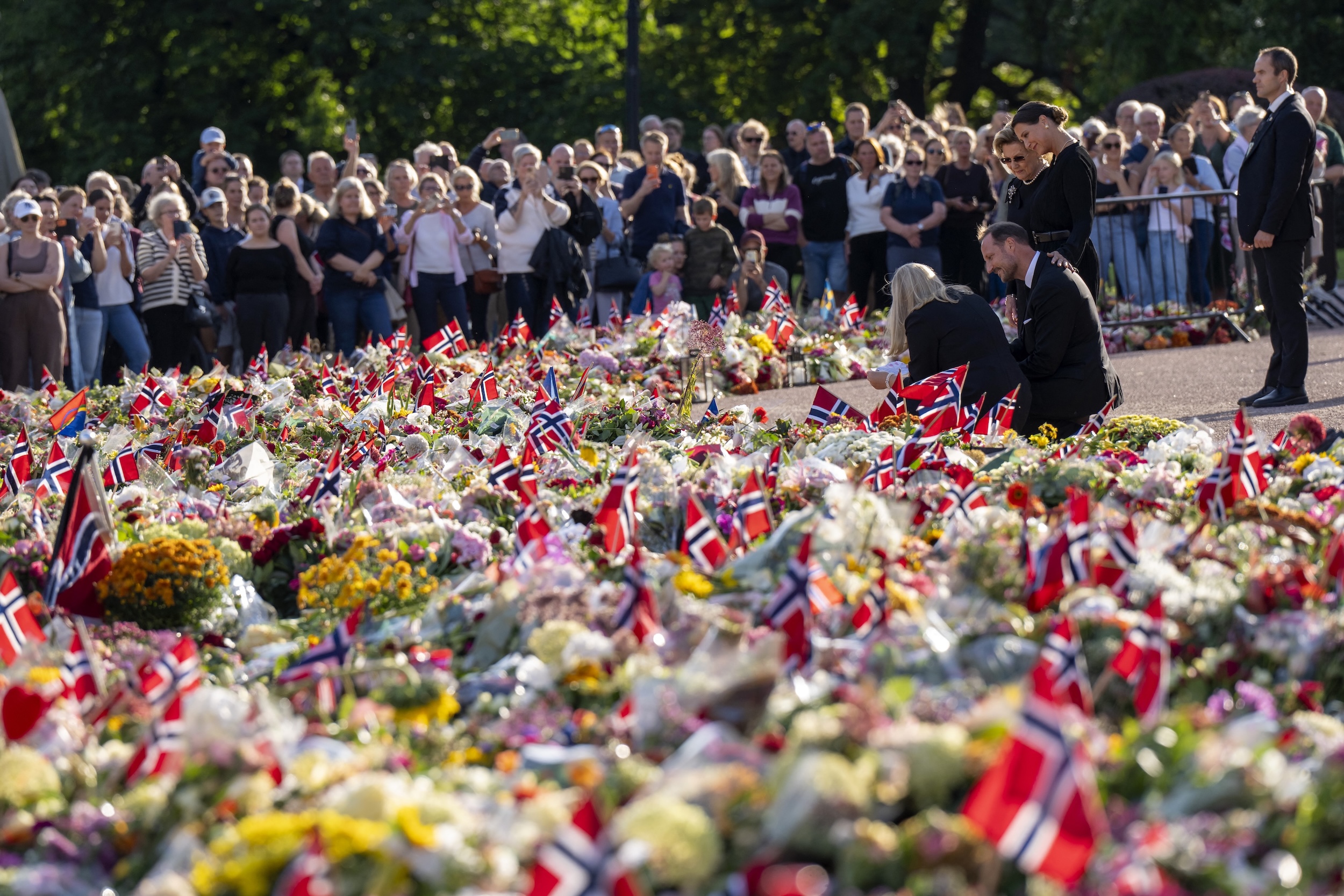 Members of the Norwegian royal family kneeling down in front of floral tributes