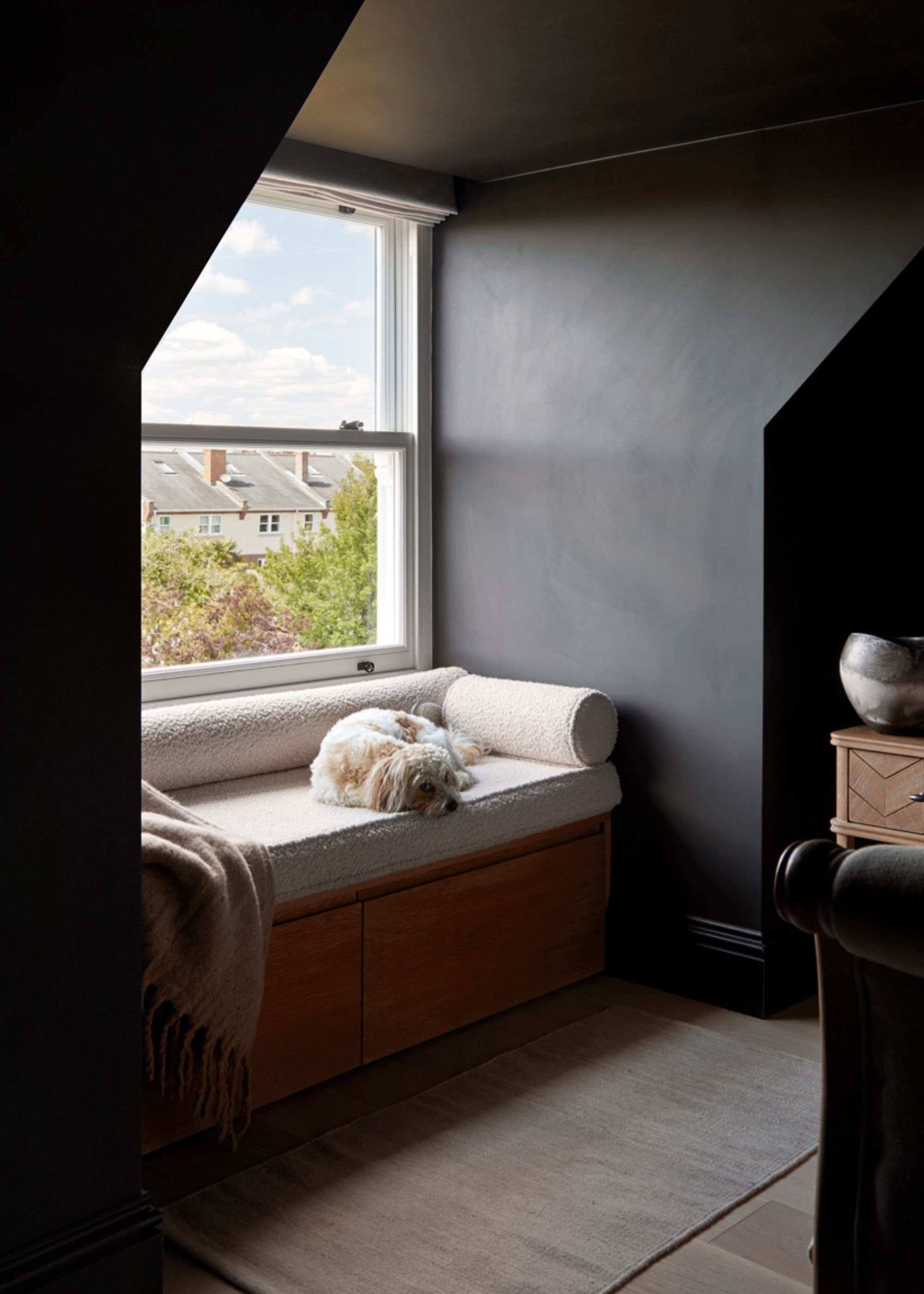 A dark bedroom a boucle bay window with a dog, and a throw