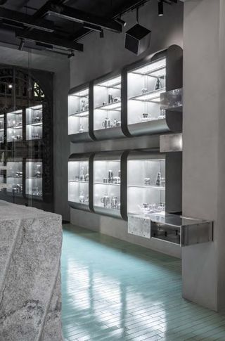 An interior of a restaurant featuring stainless steel shelves, light blue floor tiles and stone tables