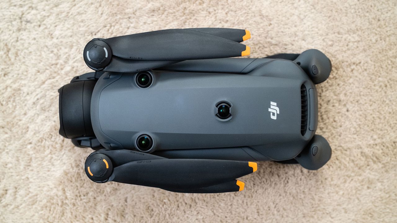 A grey drone has its propellers folded in to its side to make it more compact, is on a beige carpet.