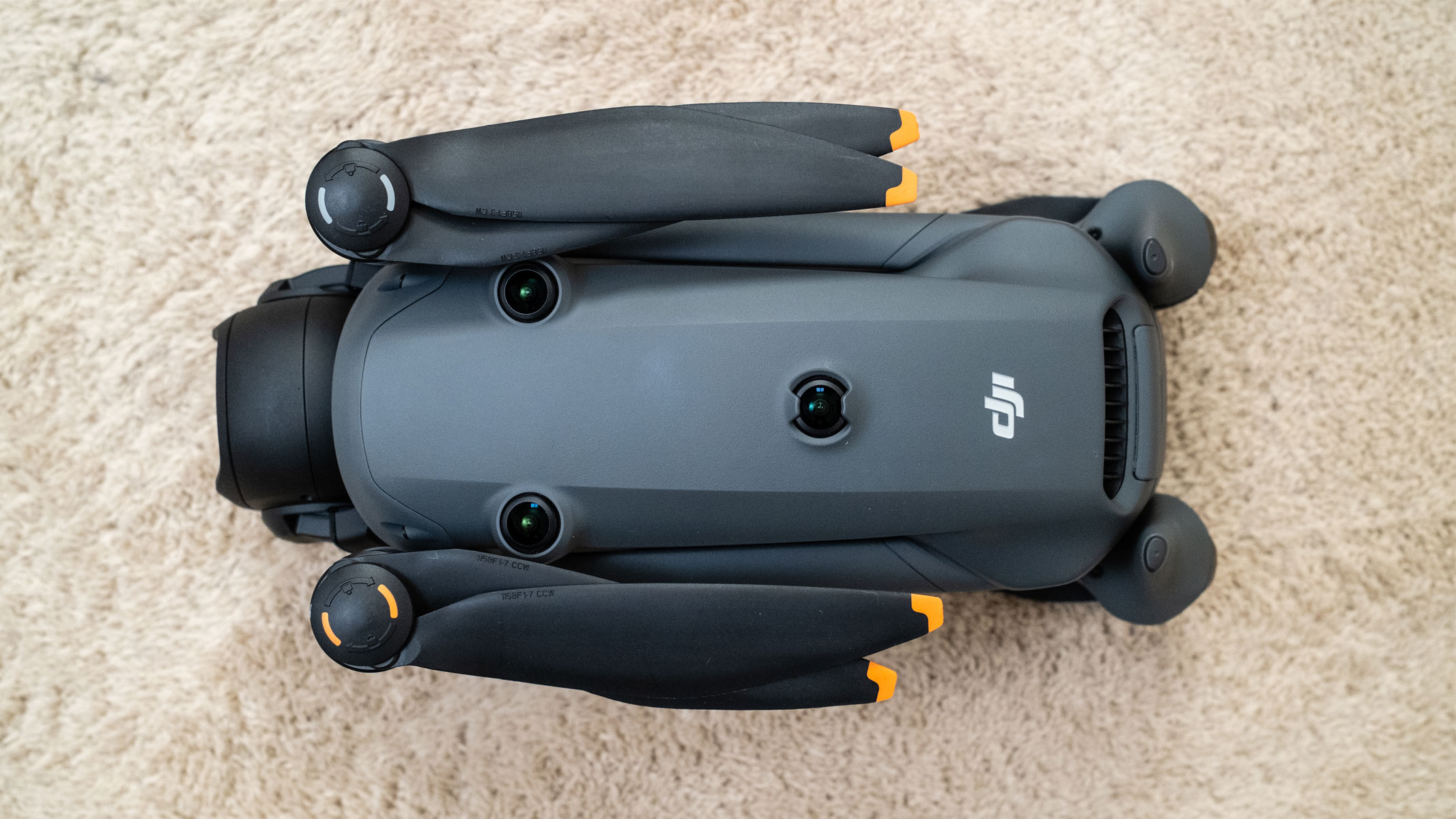 A grey drone has its propellers folded in to its side to make it more compact, is on a beige carpet.