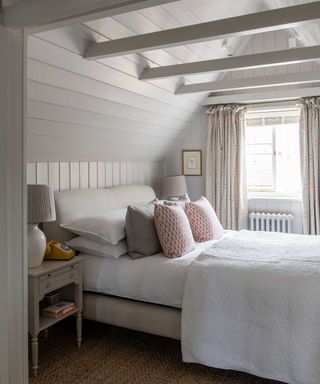 coastal bedroom with white painted wooden pannelled walls, ceiling beams and a neutral palette
