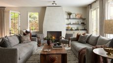 Living room with facing gray sofas, patterned pillows, a wood coffee table, curved armchairs and a fireplace beside a built-in bar.