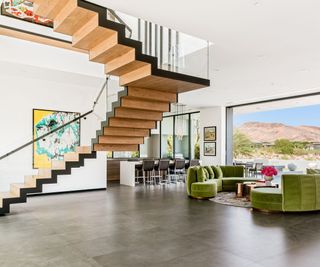 living room open plan with stairs and green sofa wide view of mountains through glass wall