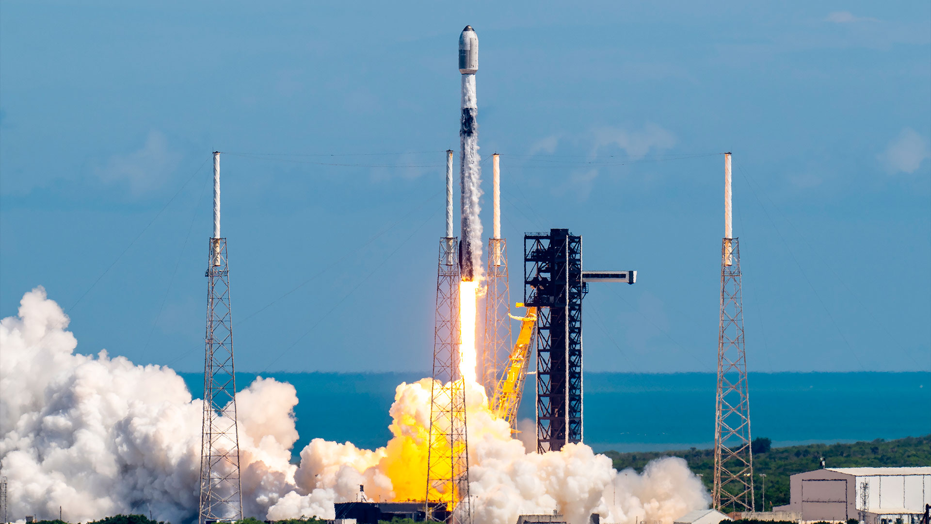 a white and black rocket lifts off into a bright blue sky