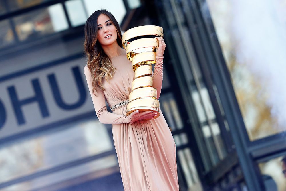 A presenter holds the Giro d'Italia trophy.