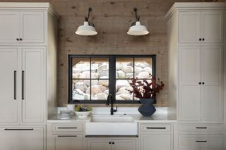 kitchen butlers sink with pale painted cabinets and black framed windows and white pendant lights