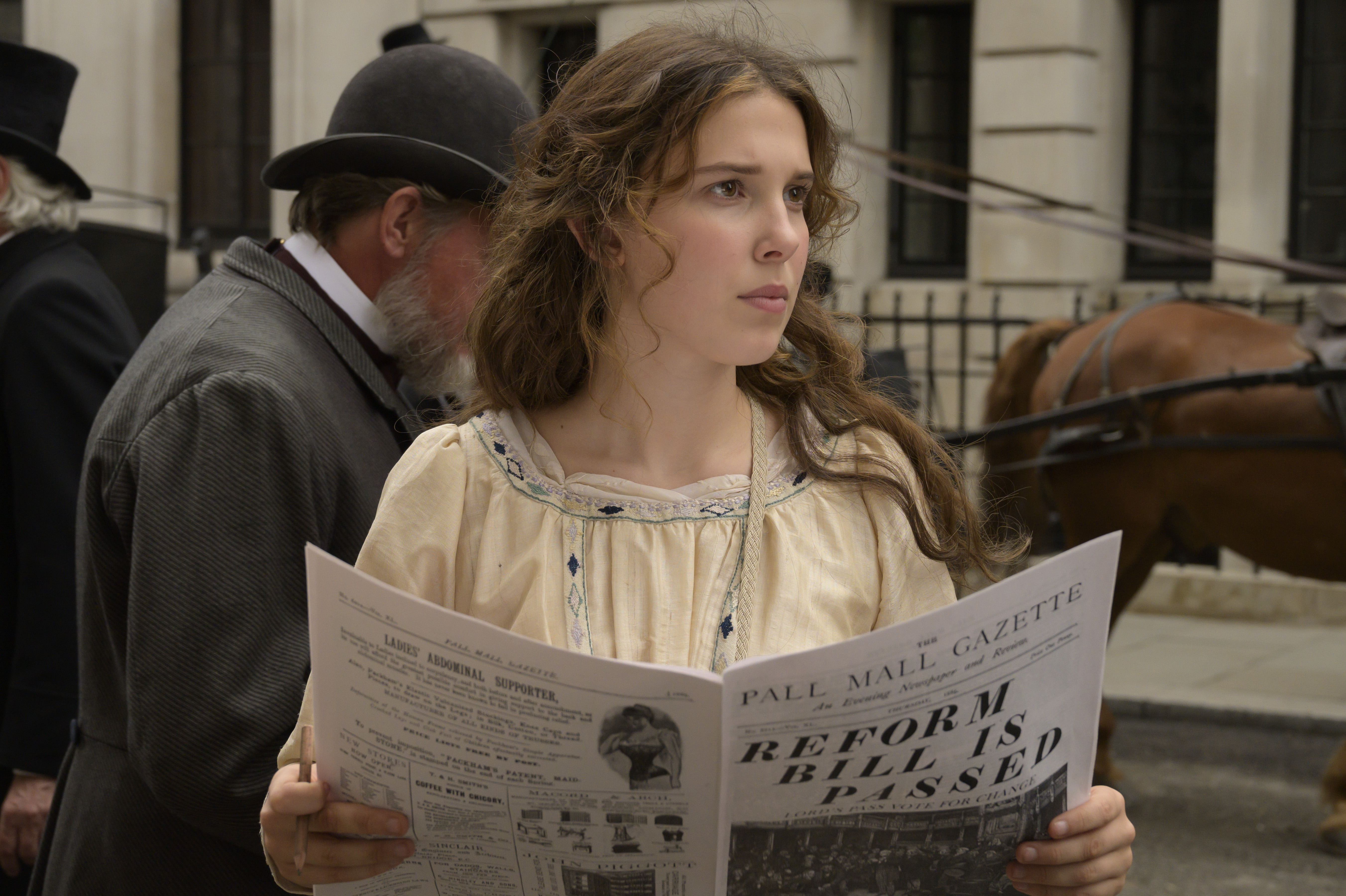 Millie Bobby Brown as enola holmes, reading a newspaper in enola holmes, one of the Best family movies on netflix