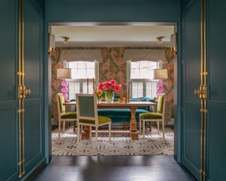 A dining room with teal green painted entrance and patterned wallpaper from Gucci