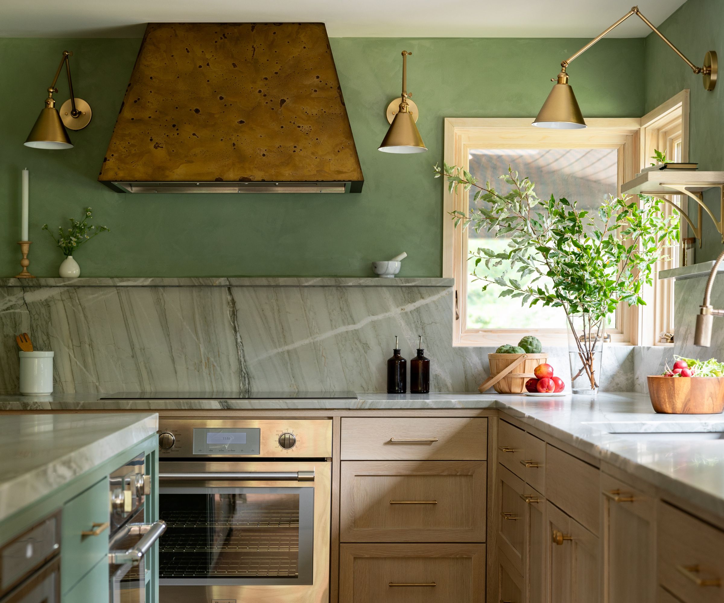 Kitchen with sage green wall, gold hood, gold oven, wall lights, and marble countertops