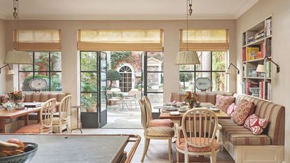 A bright breakfast nook with built-in banquette seating, patterned pillows, and large glass doors that open onto a lush garden courtyard