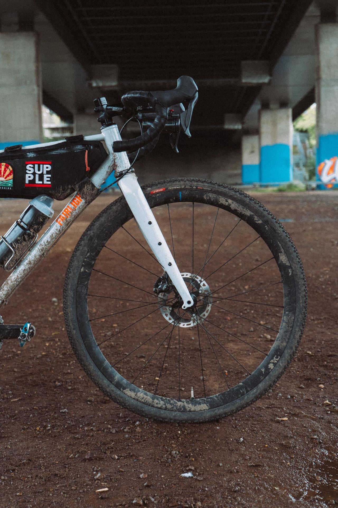 A close up of the front half of a white gravel bike under a motorway flyover