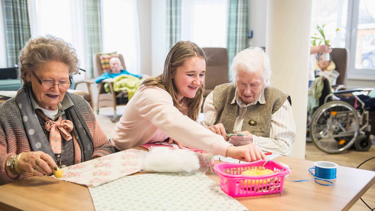 Senior women with girl doing craft activity at rest home