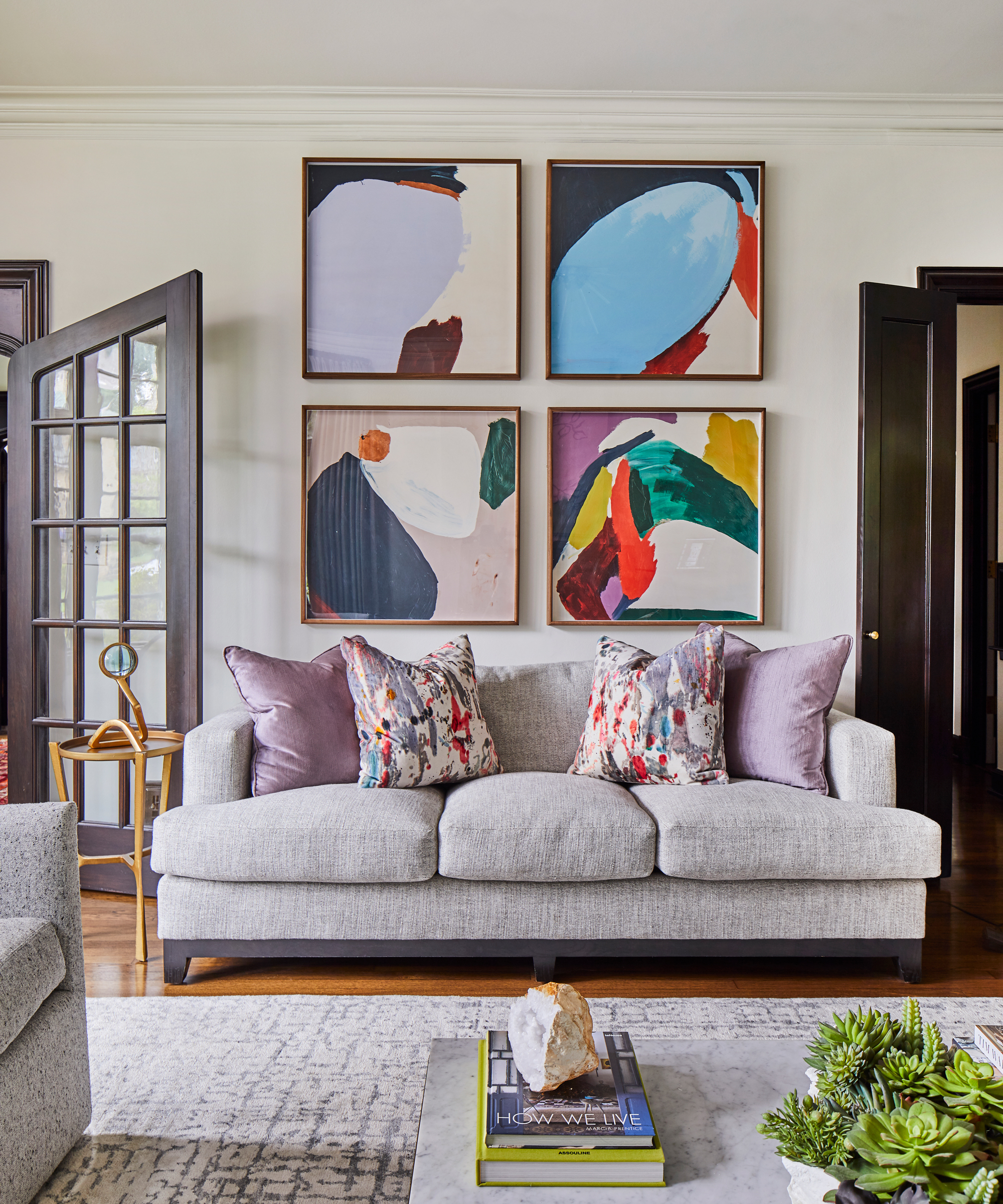 Punchy abstract gallery wall idea above grey sofa with plain and abstract scatter pillows.