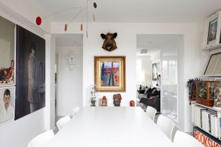 A Collector's apartment by Campbell Cadey featuring a white table and six white chairs, various tribal ornaments against a wall with a wall painting and an animal head.  