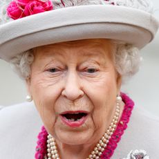 Queen Elizabeth making a shocked face wearing a gray hat and pearls