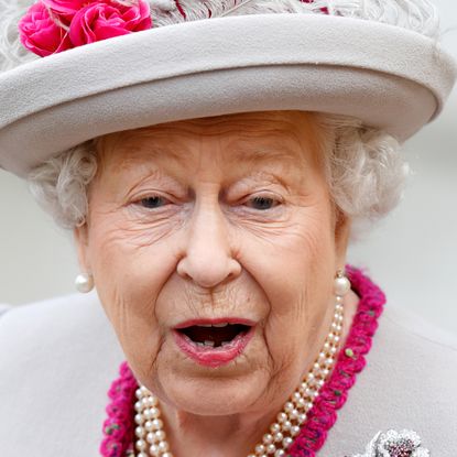 Queen Elizabeth making a shocked face wearing a gray hat and pearls