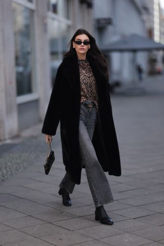 woman wearing black coat, leopard print top, jeans, and ankle boots