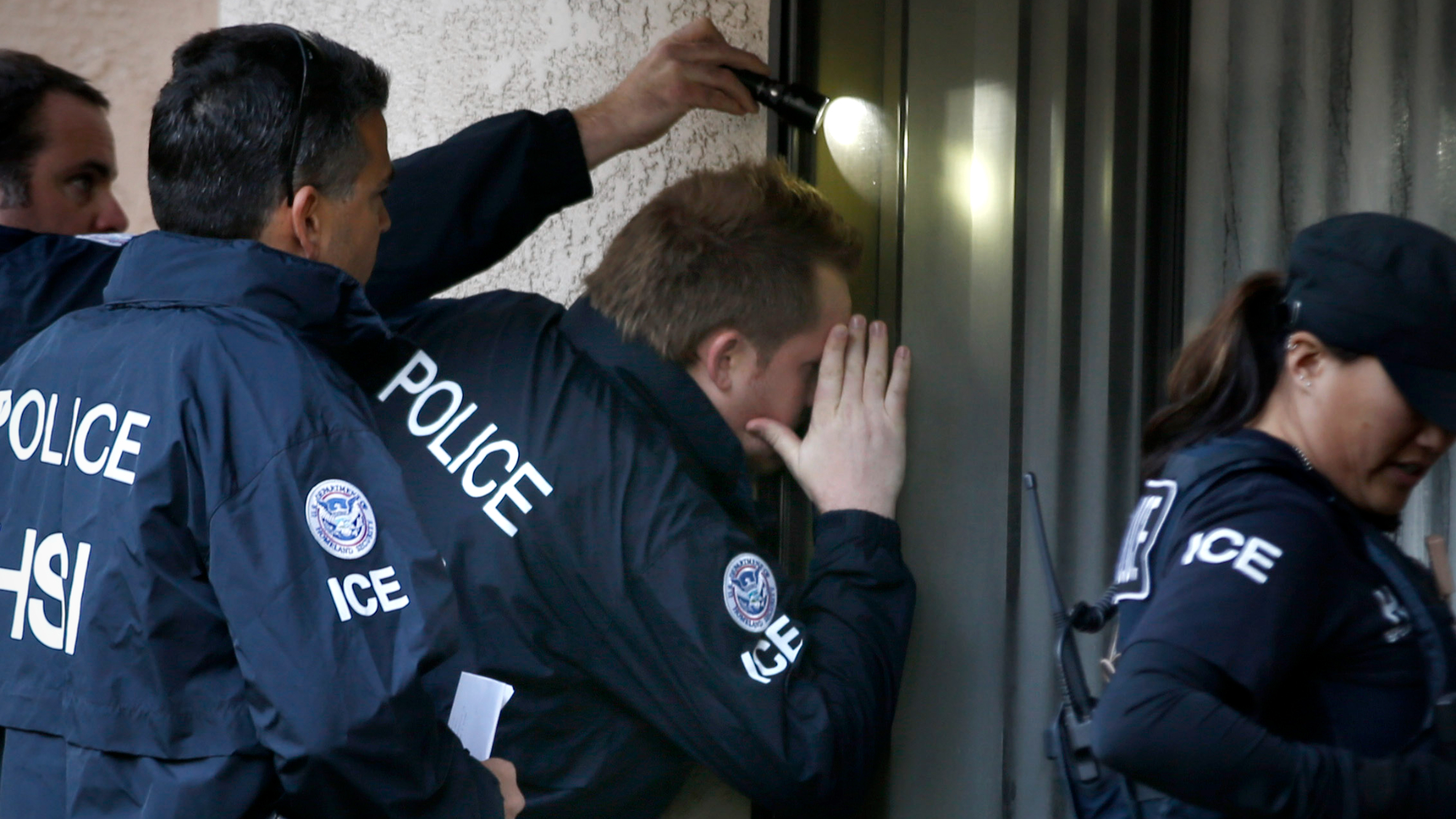 Immigration and Customs Enforcement (ICE) agents from the Department of Homeland Security look into the window of an apartment while executing search warrants in 2015.