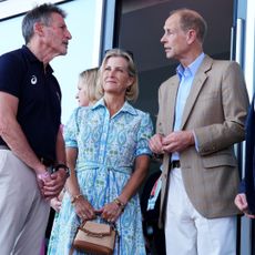 Duchess Sophie waring a blue dress clutching a straw bag next to Prince Edward