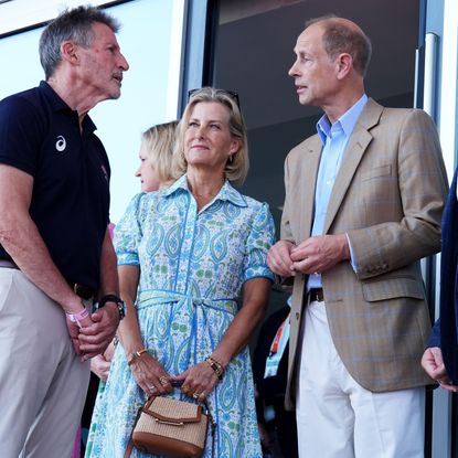 Duchess Sophie waring a blue dress clutching a straw bag next to Prince Edward