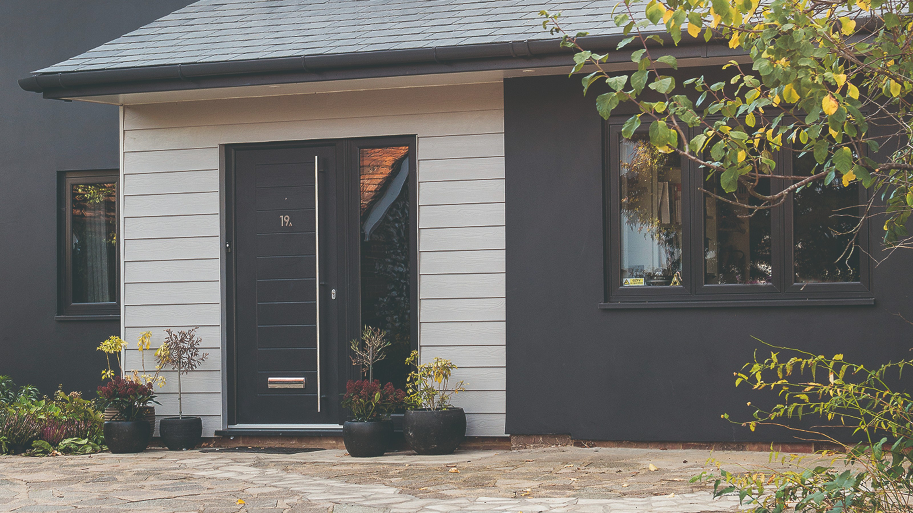 A two-tone house exterior in black and off-white with a black front door surrounded by potted plants