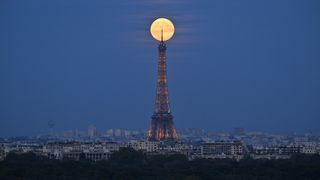 A bright full moon shines just behind the top of the Eiffel Tower in Paris.