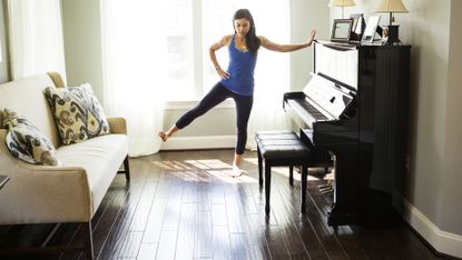 Woman leaning against a piano in front room and stretching out her leg to the side