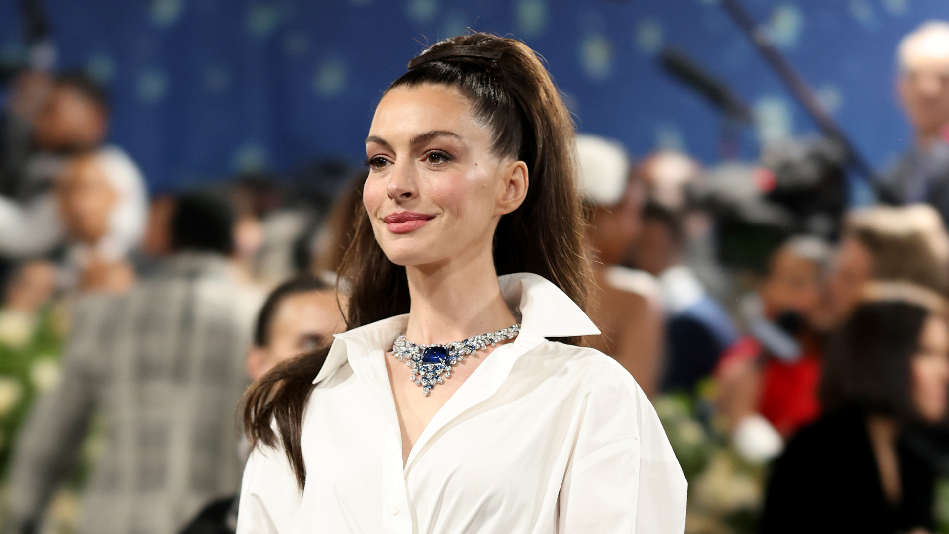 Anne Hathaway on the 2025 Met Gala steps wearing a button up shirt and capri pants