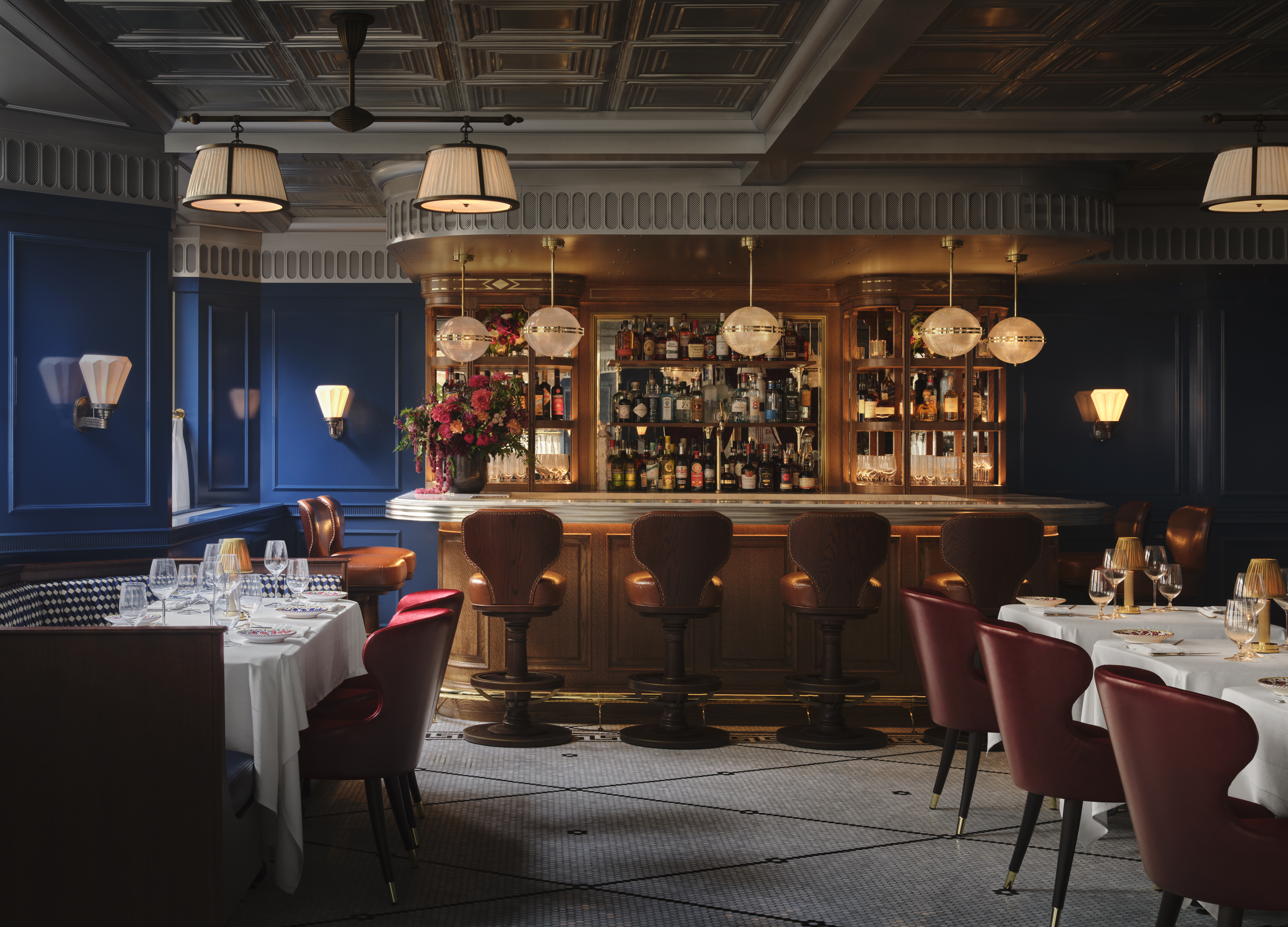 A dazzling decorated restaurant with checkered, red and white marble floors, red velvet drapery, banquettes, and leather chairs, ciambella-shaped lighting with a golden glow, and softly burning table lamps.