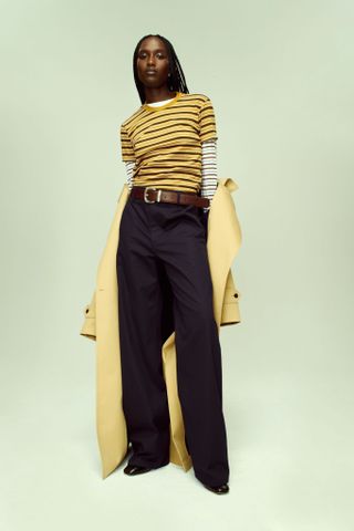 A Kallmeyer Resort 25 lookbook image showing a striped gold T-shirt with black pants and a yellow coat.