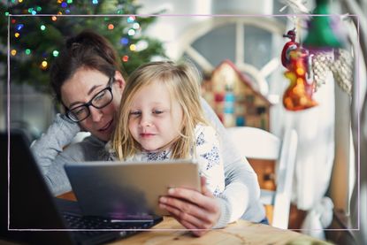 A woman and her daughter looking at a laptop with a Christmas tree in the background
