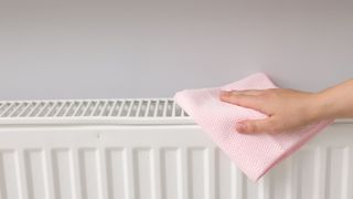 woman using a pink cloth to clean the top of a radiator
