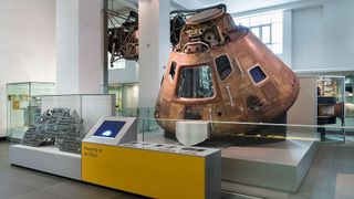 a gumdrop-shaped space capsule is displayed with other artifacts in a museum