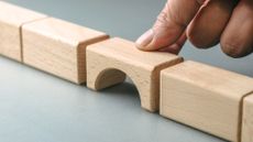A wooden block shaped like a bridge being placed between rectangular blocks in a line.