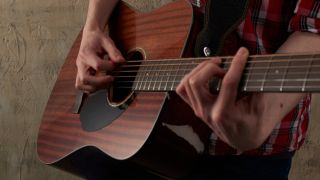 A man in a check shirt plays a barre chord on a Fender CD-60 acoustic guitar