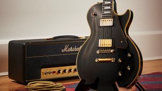 Shot of a Black Gibson Les Paul Custom with gold pickups next to a Marshall JMP MKII amp head