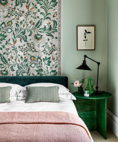 An example of how to plan bedroom lighting with a black bedside lamp on a green table next to a dark green bed