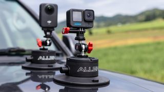 Two Allen Smart Suction Snap Camera Mounts are secured to the hood of a dark vehicle, holding a DJI action camera and a GoPro camera.