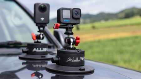 Two Allen Smart Suction Snap Camera Mounts are secured to the hood of a dark vehicle, holding a DJI action camera and a GoPro camera.